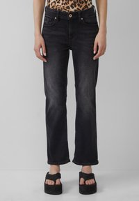 Jeans en denim noir avec une coupe droite, dotés de cinq poches et d'une fermeture à boutons. Portés avec des sandales à plateforme noires et chunky.