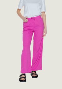 Pantaloni in lino rosa con una vestibilità ampia, dotati di un elastico in vita e di un laccetto. Abbinati a sandali neri e a una maglietta bianca semplice.