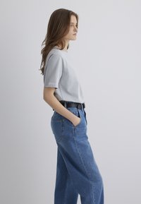 Light gray short-sleeve t-shirt paired with high-waisted blue denim jeans. The jeans have side pockets and a classic straight-leg cut.