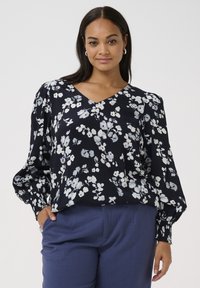 Bluză florală de culoare navy, cu modele albe și bleu deschis; decolteu în V, mâneci evazate și manșete elastice. Asortată cu pantaloni albaștri croiți.