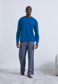 Chemise à manches longues bleue associée à un pantalon de pyjama à rayures bleu marine et blanc. La chemise a un col rond ; le pantalon est ample avec des jambes droites.