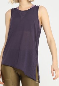 Lila ärmlös topp med en mjuk textur, med hög-låg fåll och lagerdesign, kombinerad med figurnära guldleggings.