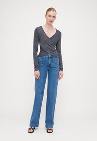 Haut enveloppant gris à manches longues en tissu texturé avec un décolleté en V profond, associé à un jean droit bleu taille haute et des sandales noires.