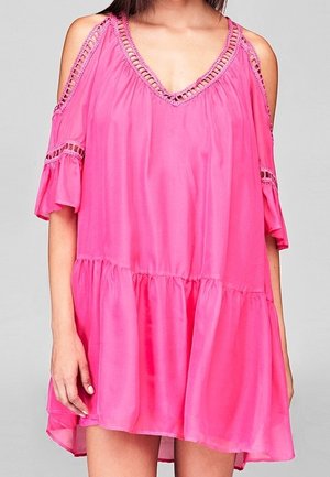 Femme portant une robe rose vif à épaules dénudées avec une bordure en dentelle et des manches courtes à volants sur un fond clair uni.
