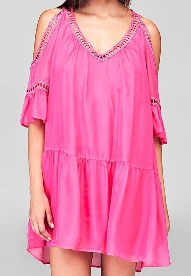 Femme portant une robe rose vif à épaules dénudées avec une bordure en dentelle et des manches courtes à volants sur un fond clair uni.