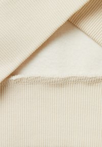 Tela de rayas beige con un suave forro de felpa crema. Presenta costuras visibles a lo largo del borde, destacando la construcción en capas.