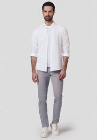 Biała koszula z guzikami noszona na jasnoszarym t-shircie, w połączeniu z jasnoszarymi spodniami i białymi sneakersami; czyste linie, minimalistyczny design.