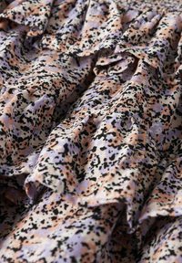 Tissu froncé dans un motif lavande, pêche et noir. Matériau léger avec une surface texturée, présentant de petites taches et un design fluide.