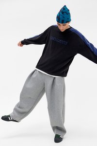 Sweatshirt oversized em corduroy preto com detalhes azuis e o texto "ETS FRANS", combinado com calças de moletão cinza folgadas e ténis pretos.