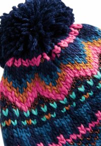 Stickad mössa med en mörk marinblå bas och ett flerfärgat zigzag-mönster i rosa, teal, orange och brunt, prydd med en stor pom-pom.