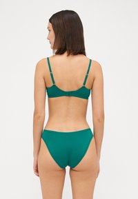 Μαγιό σε τιρκουάζ απόχρωση που περιλαμβάνει στηθόδεσπο με δομημένη εφαρμογή, ρυθμιζόμενους ιμάντες και κούμπωμα, συνδυασμένο με ψηλόμεσα σλιπ. Απαλή υφή.