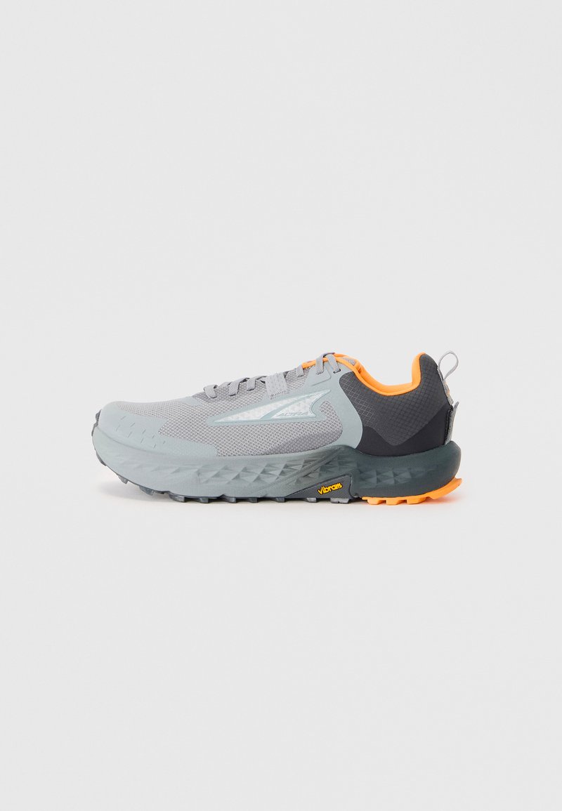 Lys grå atletisk sko med mesh-overdel, orange accenter og en textured mørkegrå hæl. Har en robust ydersål med Vibram-branding.