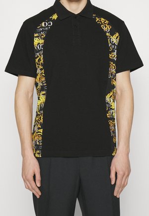 Black short-sleeve polo shirt with golden baroque patterns and white text on side panels, worn by a standing person with arms relaxed.