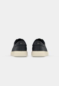 Zapatillas de cuero negro con acabado texturizado, con una suela de goma crema y pequeños detalles en el talón.