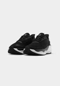 Scarpe sportive nere con una parte superiore testurizzata, design con lacci, suola bianca spessa e suola in gomma con un motivo di presa testurizzato.
