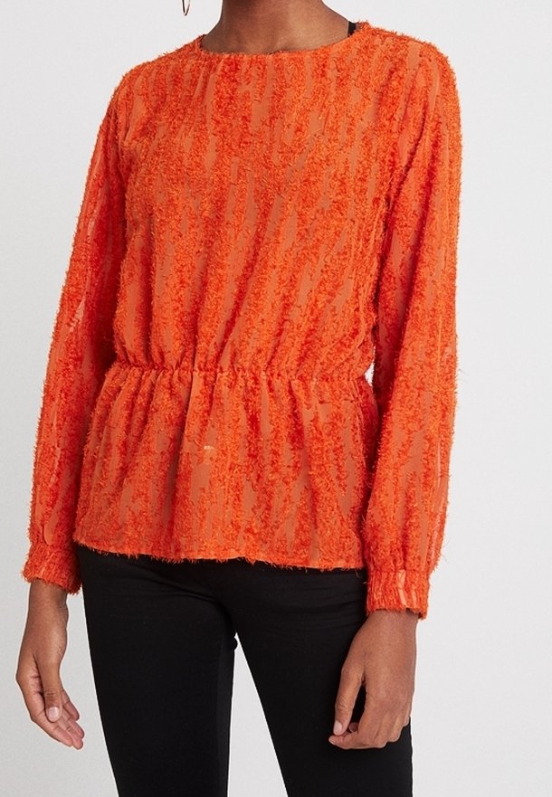 Transparente orange Bluse mit strukturierten Streifen, langen Ärmeln und elastischem Bund. Kombiniert mit schwarzen Hosen, die einen lässigen Schnitt zeigen.