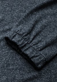 Mörkgrå stickad långärmad tröja med en strukturerad, melerad mönstring. Har samlade ärmslut med elastiska detaljer. Mjuk tygfinish.