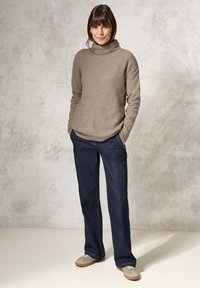 Beige ribbad stickad polotröja i kombination med mörkblå vida jeans och ljusgrå mockaskor. Slät textur och avslappnad passform.