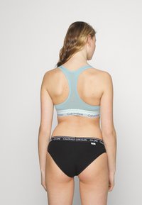 Ljusblå sportbh med racerback-design, med ett vitt Calvin Klein-logoband. Svarta baddräktsbottoms med ett vitt CK one-logoband.