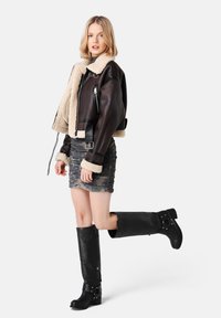 Brown leather aviator jacket with cream shearling lining, fitted gray ruched skirt, and tall black leather knee-high boots with buckles.