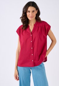 Camicia rossa a maniche corte con chiusura a bottoni e scollo a V. Realizzata in tessuto leggero, presenta una vestibilità comoda e dettagli di arricciatura discreti.