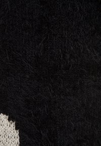 Gros plan sur un tissu noir duveteux avec des boucles et des vagues texturées, montrant un détail de tricot doux et dense avec une petite zone de tissu tricoté beige sur le bord.