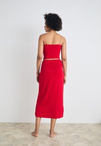 Conjunto rojo de dos piezas que incluye un top corto ajustado con tirantes finos y una falda fluida de longitud tobillo, fabricada con una tela suave y elástica.