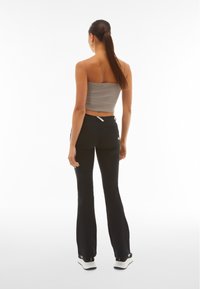 Mustat leveälahkeiset housut, joissa on tyylikäs muotoilu ja etutaskut, yhdistettyinä tiukkaan harmaaseen lyhythihaiseen paitaan, jossa on ohuet hihnat ja ribbikuvio.