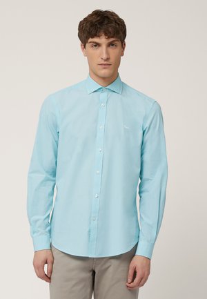 Lichtblauwe overhemd met lange mouwen en een button-down kraag, witte knopen en een klein geborduurd logo op de linkerkant van de borst. Katoenen stof, gladde textuur.