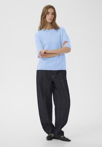 Helehall sinise lühikeste varrukatega pehme kootud kampsun, kombineeritud lahtiste tumedate teksapükstega tugeva õmblusega ning mustade sussidega.