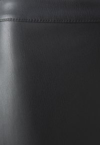 Černá kožená textura s jemným, mírně zrnitým povrchem. Viditelné stehy podél okrajů zdůrazňují její elegantní design.