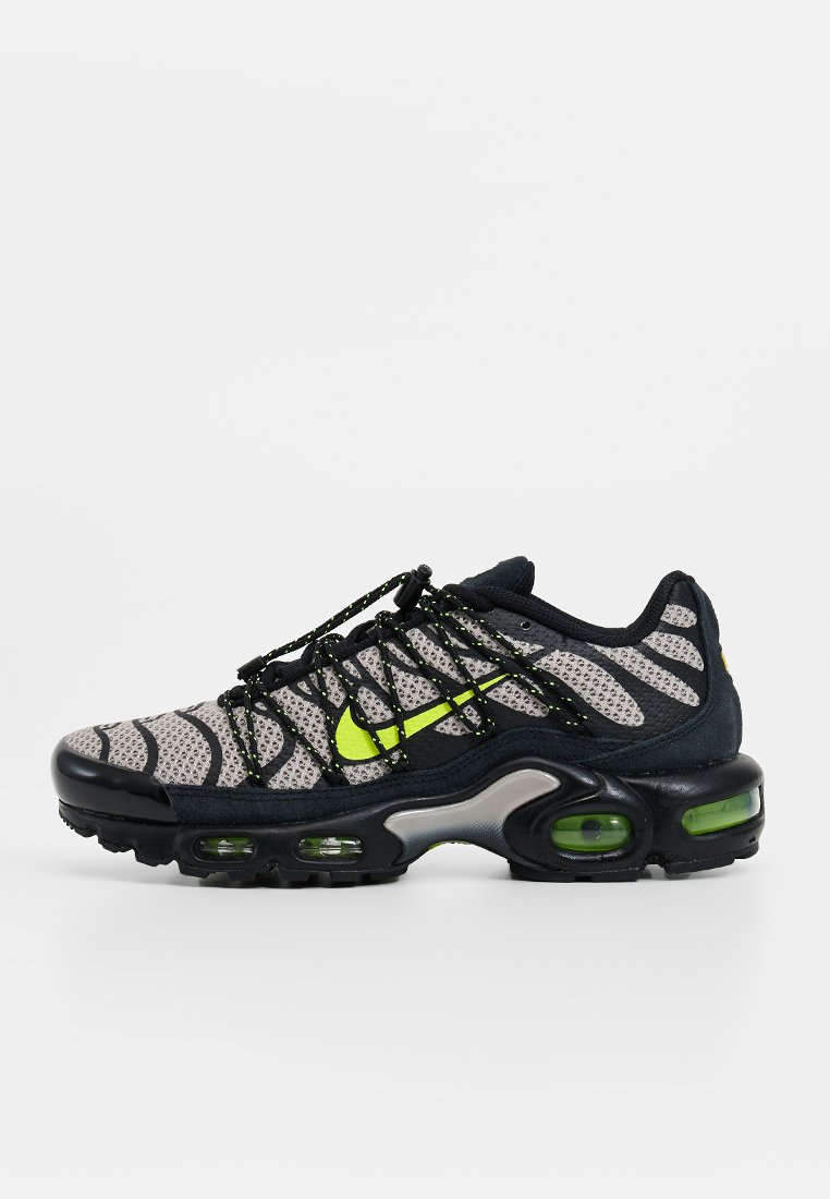 Sneaker sportivo con una tomaia in mesh nera e grigia, dettagli in verde neon, motivi testurizzati e pod di ammortizzazione visibili sulla suola.