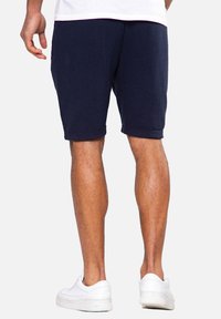 Marineblaue Shorts aus strukturiertem Stoff mit geripptem Design, endend auf Oberschenkelmitte, kombiniert mit weißen Turnschuhen.