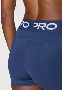 Σκούρο μπλε ναυτικό αθλητικό σορτς με απαλό ζωνάρι μέσ ης που φέρει το λογότυπο "PRO" σε λευκό κείμενο. Λείο ύφασμα με καθαρές ραφές και χωρίς ορατά σχέδια.