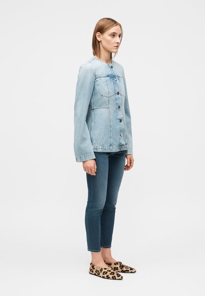 Veste en denim bleu clair avec un devant à boutons et deux poches poitrine, associée à un jean skinny en denim foncé et des chaussures à enfiler à imprimé léopard.