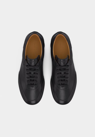 Ζευγάρι μαύρα δερμάτινα αθλητικά παπούτσια με κορδόνια και καφέ εσωτερική επένδυση, φωτισμένα από πάνω σε λευκό φόντο.