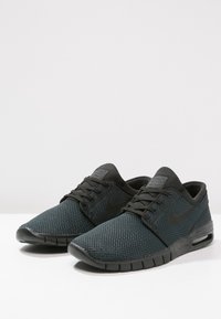 Nike-sneakers i mörkgrå mesh med svarta accenter. Har en låg profil, rund tå och texturerad yta. Snördesign med vadderad krage.