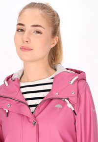 Giacca impermeabile rosa con cappuccio grigio, chiusura con zip e accessori in metallo argentato. Presenta un logo a ombrello e un cordoncino al collo.