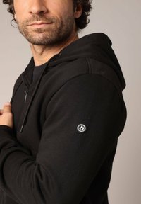 Zwarte ritshoodie van een katoenmix, met een capuchon, textuurstof en een ronde logopatch op de linkermouw.