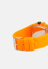 Orange silikon armbandsur med en texturerad yta, silverspänne och genomskinlig baksida som avslöjar den orange urtavlan och svarta krona.