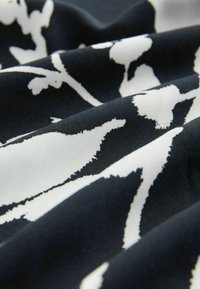 Schwarzer Stoff mit einem weißen Blumenmuster, der eine glatte Textur und ein fließendes Aussehen hat und die Kontraste zwischen den Farben betont.