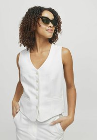Biała bezrękawnik z dekoltem w serek, pięcioma guzikami z przodu i bocznymi kieszeniami, w połączeniu z ciemnymi okularami przeciwsłonecznymi, charakteryzująca się gładką teksturą.