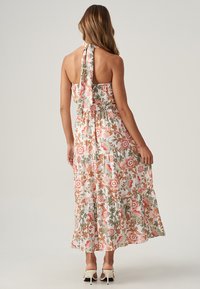 Robe maxi florale en tissu léger avec un col halter, ornée d'un motif floral rose et vert, et de volants superposés le long de la jupe.
