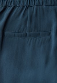 Tessuto blu scuro con una texture liscia e una vita arricciata, con una tasca posteriore piatta e discreta.