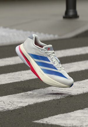 Zapatilla ligera para correr con una parte superior blanca texturizada con franjas azules, suela con acento rojo y un diseño de punta redondeada y lisa.