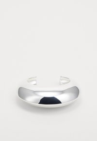 Brazalete de cuff de metal plateado con una superficie lisa y reflectante, extremos abiertos y un diseño redondeado y minimalista.