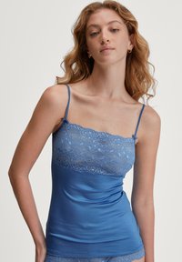 Blauwe satijnen camisole met kantafwerking aan de bovenkant, voorzien van dunne verstelbare bandjes en een getailleerde silhouet. De textuur lijkt glad en zacht.