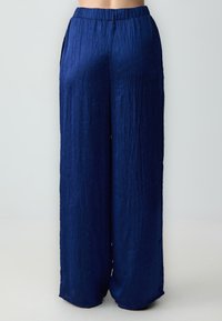 Navyblauwe wijd-gelimiteerde broeken van gekreukeld stof, met een elastische tailleband en een gladde textuur. Geen zichtbare zakken.