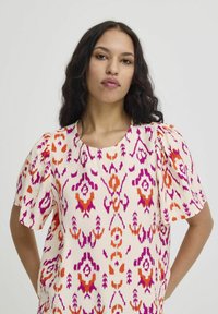 Lightweight, cream blouse with vibrant purple and orange ikat patterns, short puff sleeves, and a rounded neckline. Textured fabric.