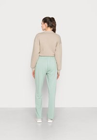 Sweatshirt oversized bege emparelhado com calças de corrida verde menta claras, com faixa elástica na cintura e corte casual. Cor sólida clara, textura suave.